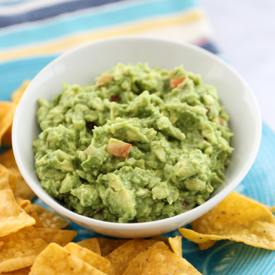 guacamole in a white bowl surrounded by chips