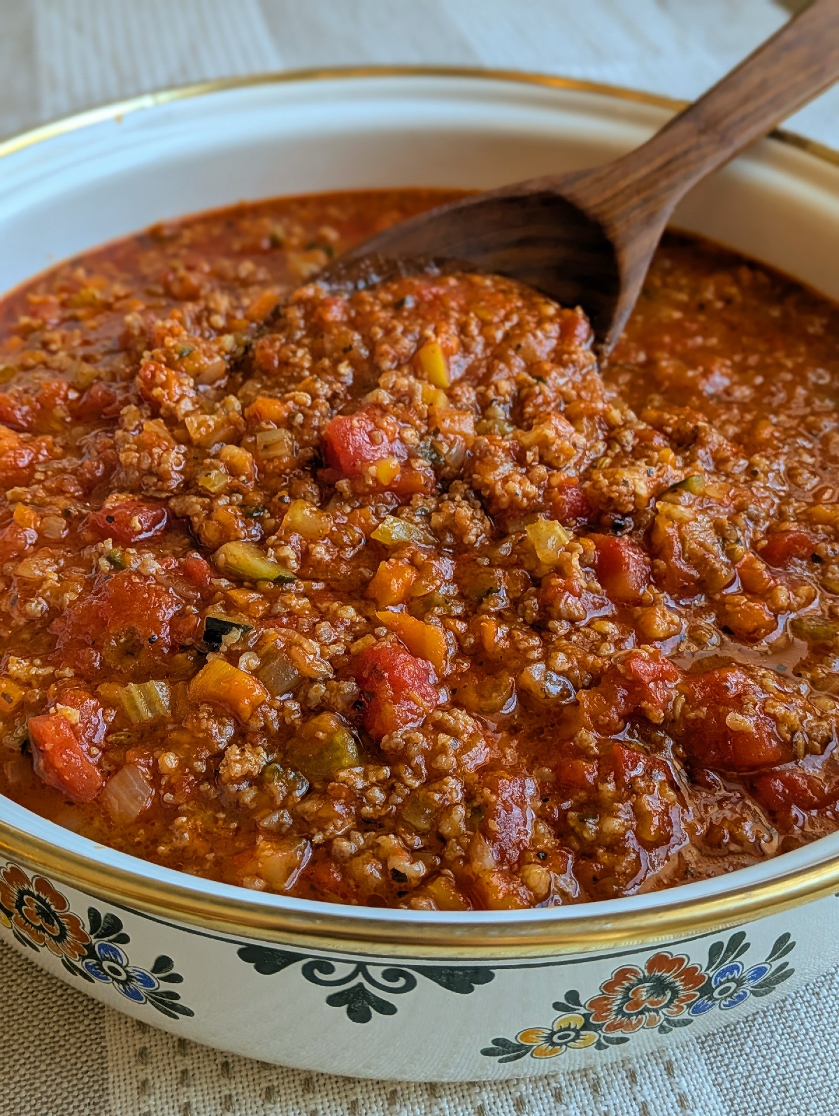 A pot full of veggie-packed pasta sauce with a wooden spoon in it.
