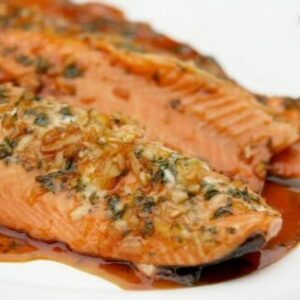 A closeup of Orange Teriyaki Salmon with teriyaki sauce spilling onto a white serving dish.
