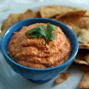 A small bowl filled with toasted red pepper hummus, surrounded by pita chips.