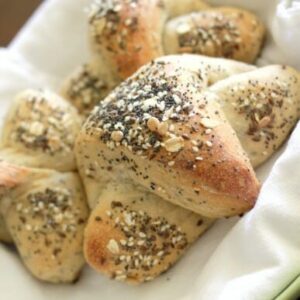 A basket filled with crescent shaped rolls, topped with seeds.