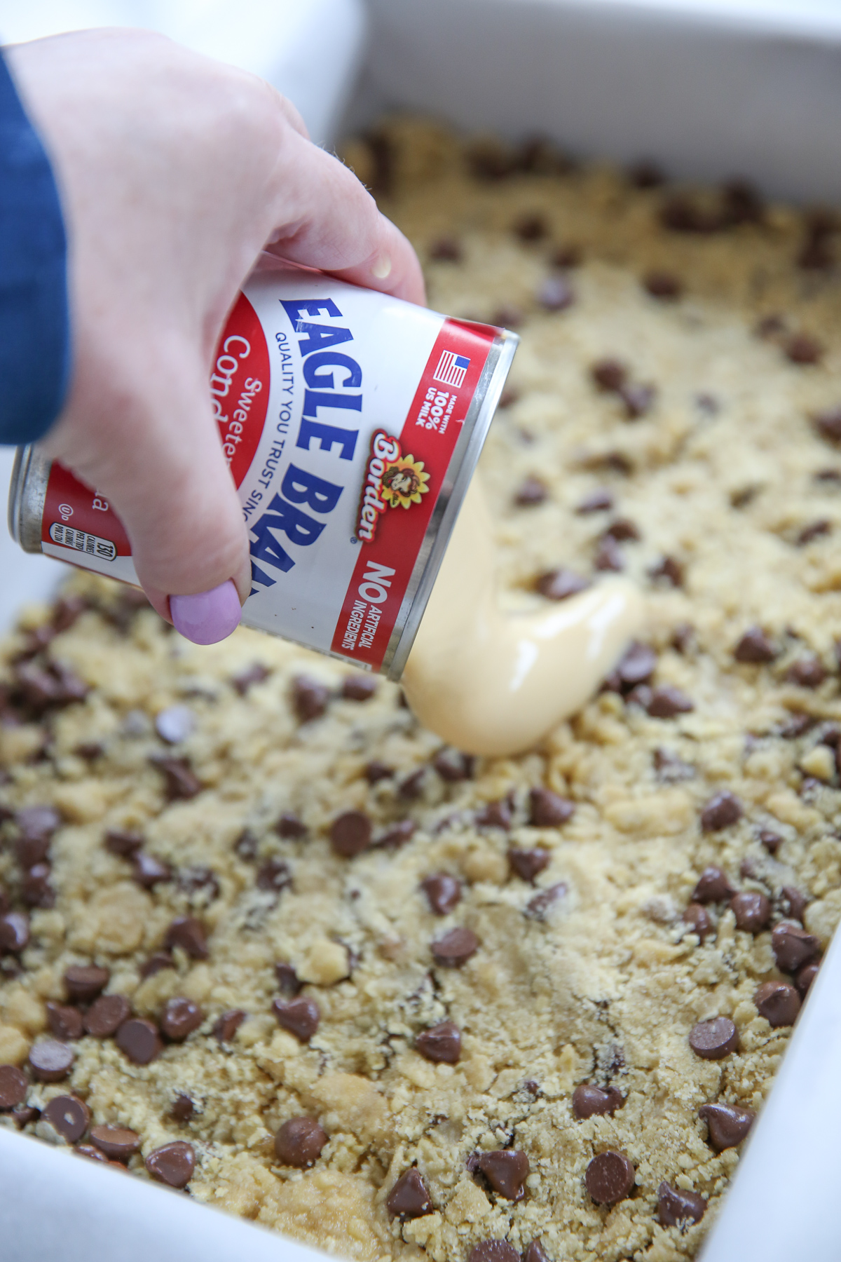 pouring sweetened condensed milk onto cookie bars