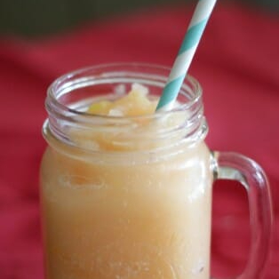 Slushy peach punch in a glass with a teal and white striped straw.