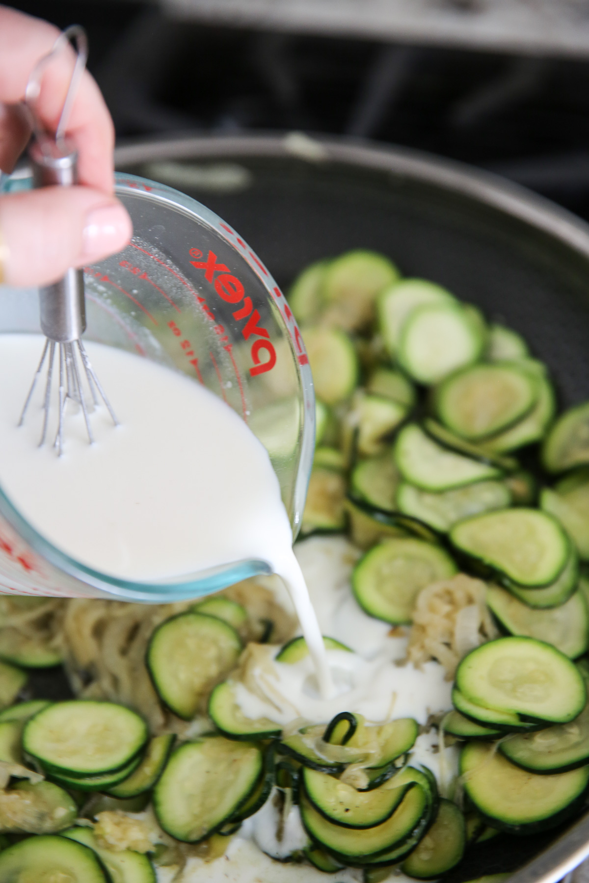 pouring cream into a pan of zucchini
