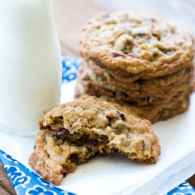 A chocolate cranberry coconut cookie, broken in half and laying in front of a stack of cookies and a glass of milk.