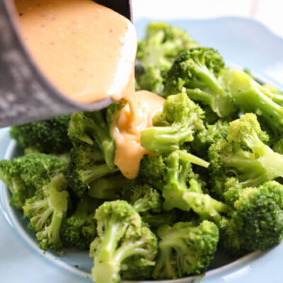 Cheese sauce being poured over a plate of steamed broccoli.
