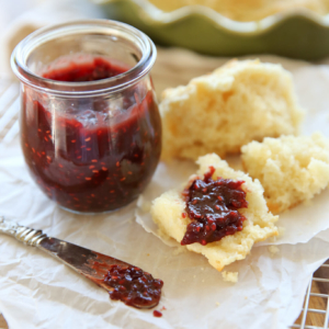 A little glass pot full of raspberry chocolate jam, with a jam covered biscuit piece next to it.