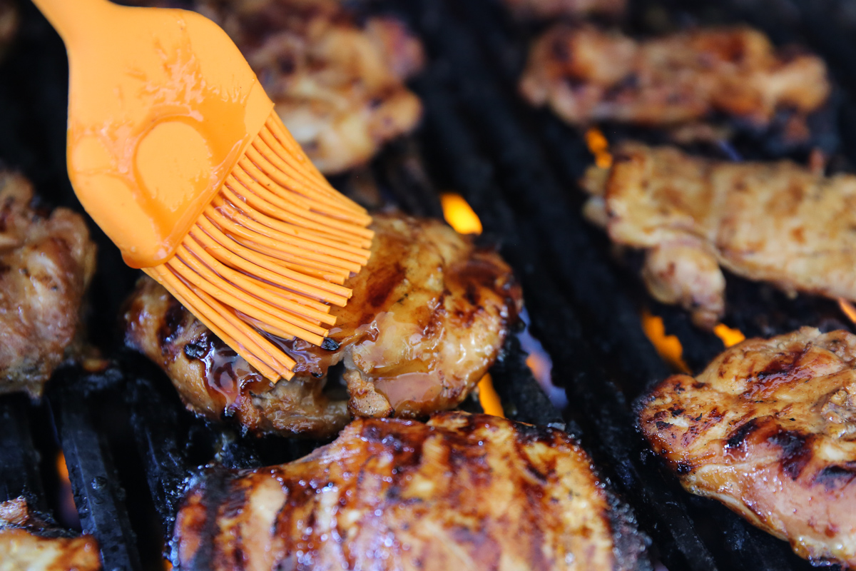 Basting chicken thighs on the grill.