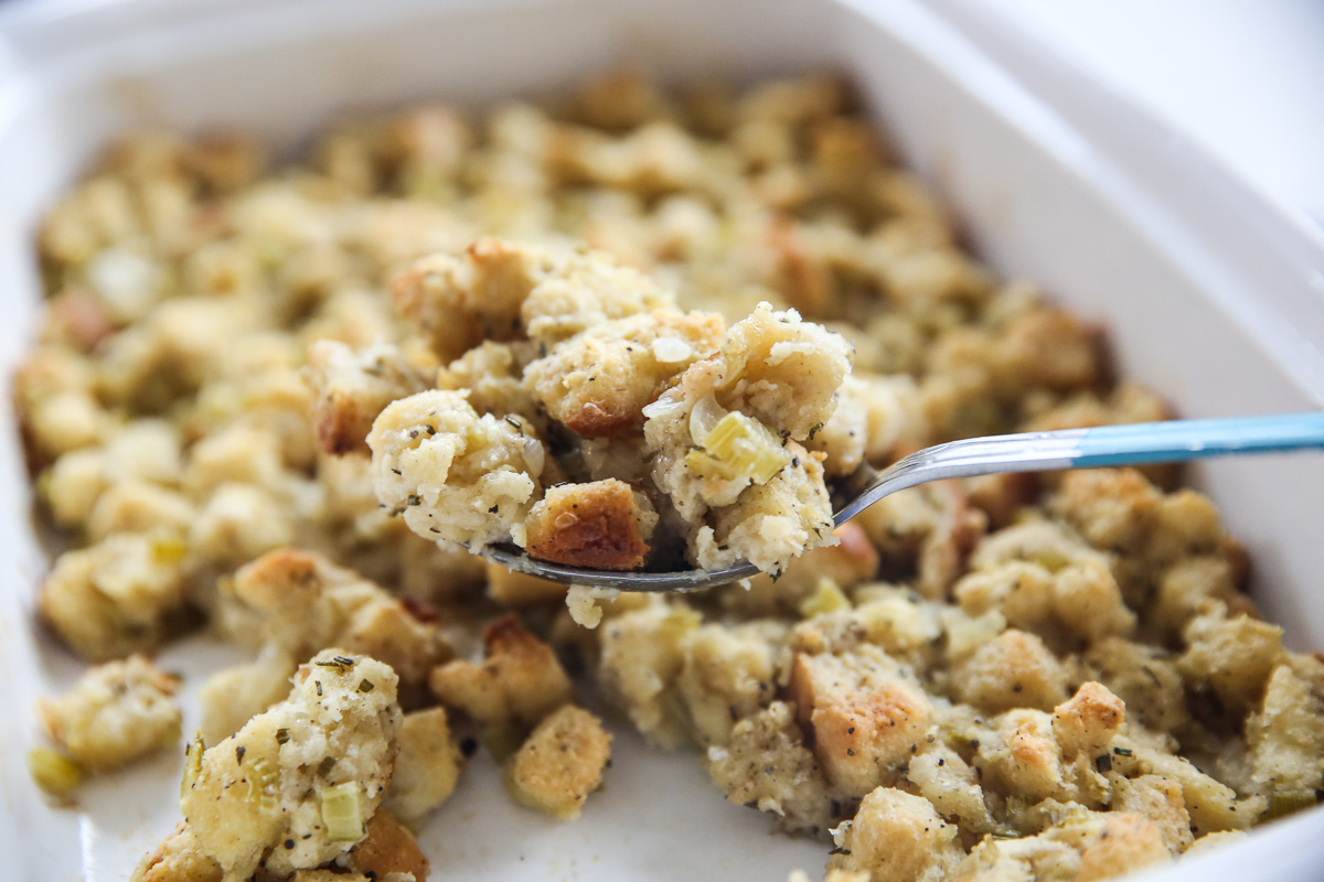 stuffing on a serving spoon in a white baking dish
