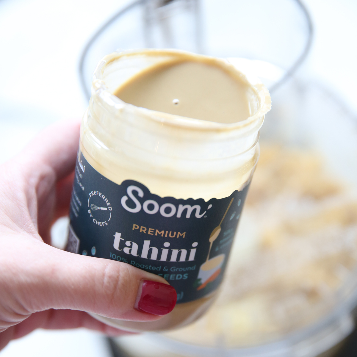 hand holding tahini over blended chickpeas