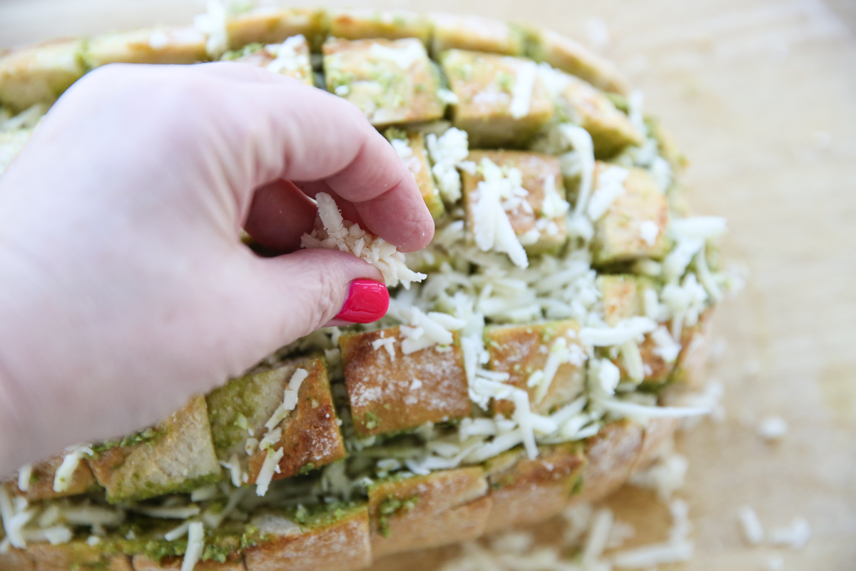 sprinkling cheese onto bread with pesto
