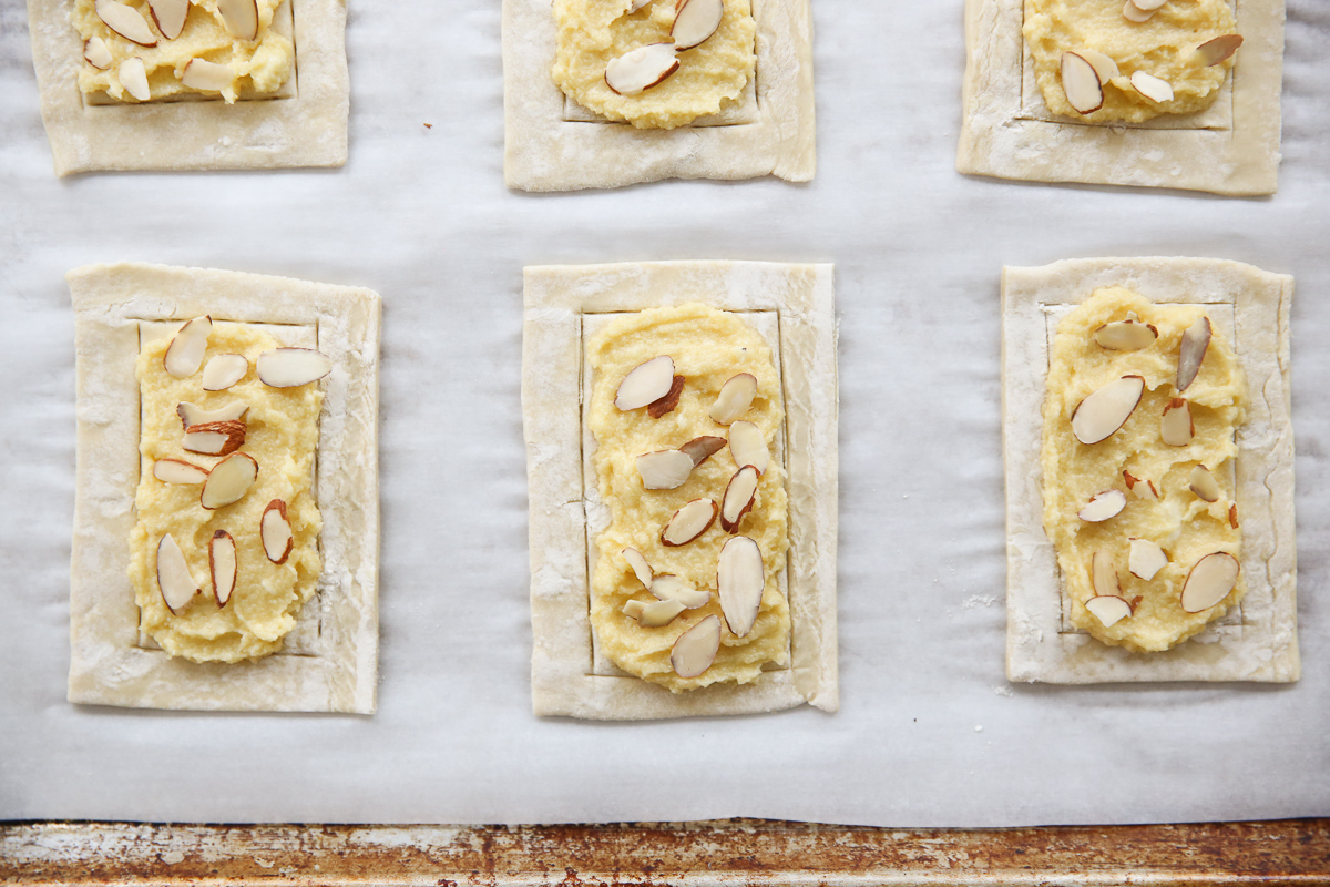 puff pastry cut into small pieces on a cookie sheet with almond filling and sliced almonds before baking
