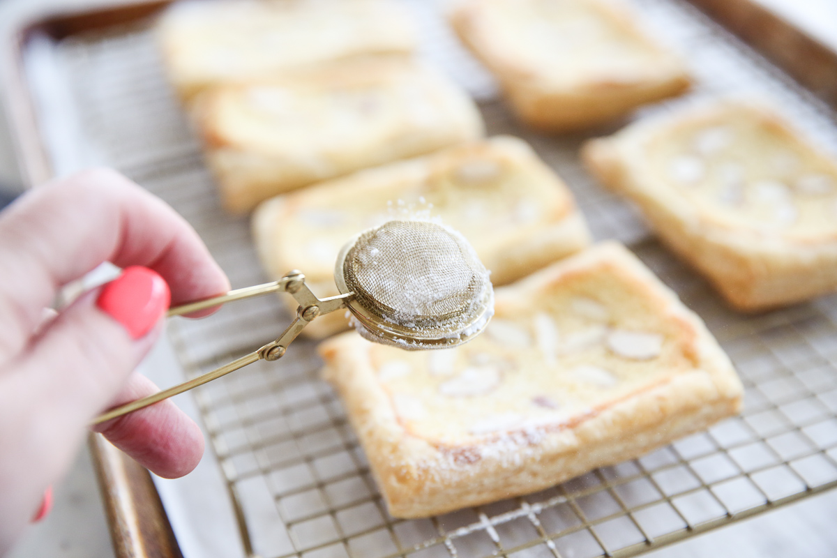 sprinkling powdered sugar over baked almond pastries