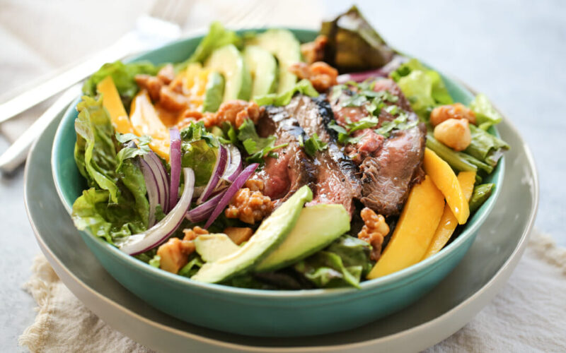 salad bowl with sliced steak and fresh mangoes